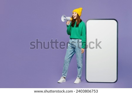 Full body young woman she wear green sweater yellow hat casual clothes big huge blank screen mobile cell phone smartphone with area scream in megaphone isolated on plain pastel light purple background