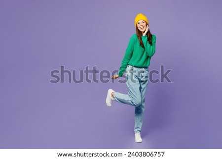 Full body side view young woman she wear green sweater yellow hat casual clothes hold put hand on face look camera isolated on plain pastel light purple background studio portrait. Lifestyle concept