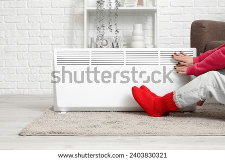 Young woman in warm winter socks near electric heater. Concept of heating season Royalty-Free Stock Photo #2403830321
