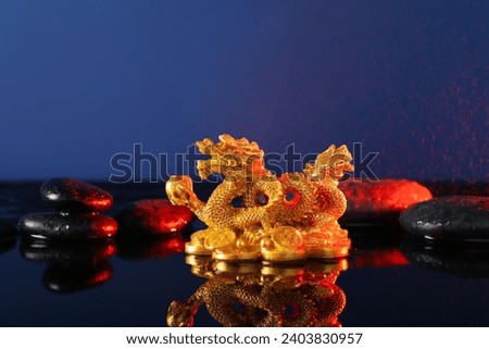 Golden Chinese dragon figurine with pebbles and water droplets on reflective surface against blue background. New Year celebration