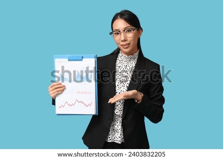 Portrait of young Asian businesswoman showing charts on blue background