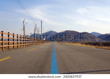 Yeoju City, South Korea - February 20, 2020: A ground-level perspective of the Hangang Bike Path, with its distinctive blue center lane, set against a backdrop of imposing hills.
