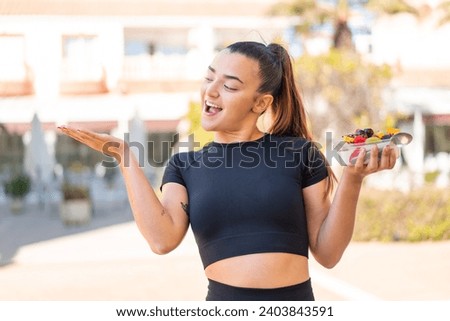 Young pretty brunette woman holding a bowl of fruit at outdoors with surprise facial expression