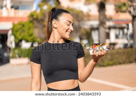 Young pretty brunette woman holding a bowl of fruit at outdoors