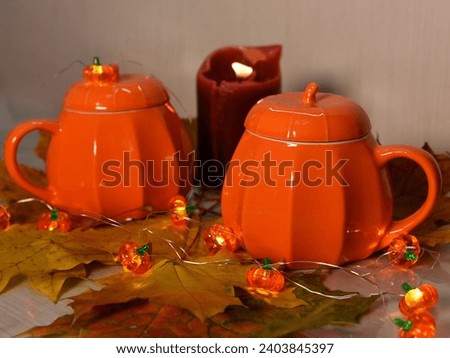 Two pumpkin mugs, glowing garlands and a burning candle. Autumn atmosphere.
