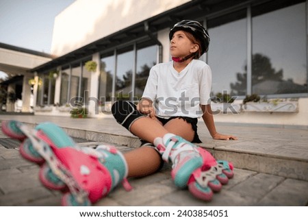 Roller skating teen in outdoors on inline skates sitting on road, low angle. Caucasian young girl training in outdoor. Copy space