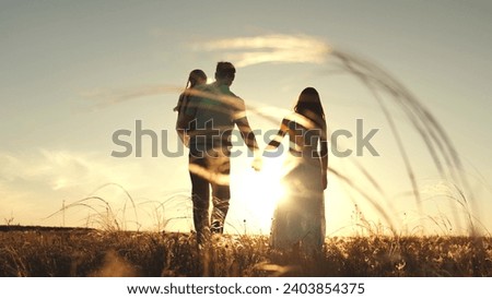 Silhouette of couple with daughter sitting in father arms walking in field in evening. Silhouette of married couple walking in field with daughter in arms. Father and mother with child walk at sunset