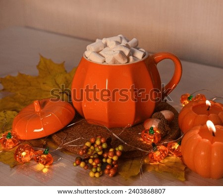 Orange pumpkin mug with drink and marshmallows. Burning orange pumpkins and yellow maple leaves.