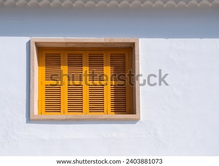 Small window with yellow wooden shutters on a white wall.