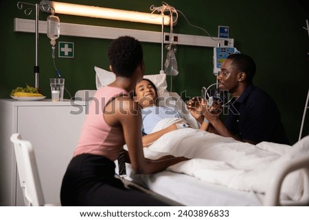 Happy parents chat by daughter's bedside in hospital. Royalty-Free Stock Photo #2403896833