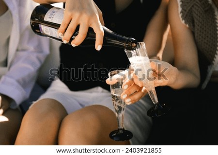 girls pour champagne from a bottle into plastic cups close-up bachelorette party