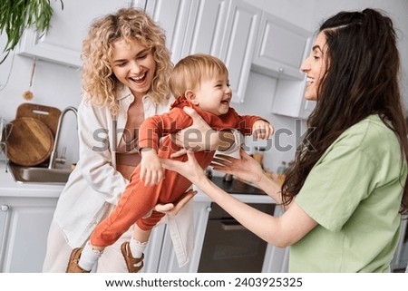 good looking jolly lgbt couple spending time together with their toddler daughter, modern parenting Royalty-Free Stock Photo #2403925325