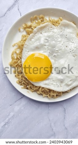 Tasty Fried noodle (Indomie Goreng) with sunny fried egg, served on white plate



