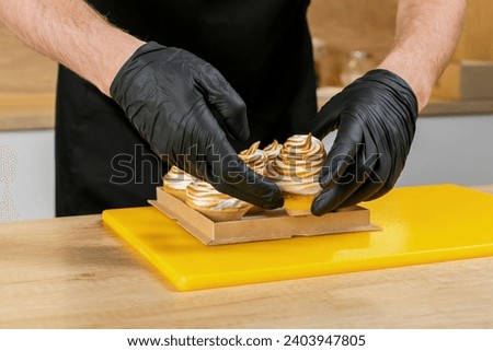 Person in black gloves arranging lemon meringue tarts on a cardboard tray, concept related to pastry making or dessert presentation