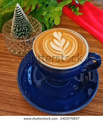 Close up picture of latte art hot cappuccino in a blue cup with Christmas decoration as the background
