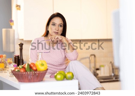  woman sitting on her kitchen counter while holding cellphone.