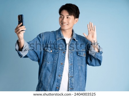 Portrait of an Asian guy wearing a jacket and using a phone posing on a blue background Royalty-Free Stock Photo #2404003525