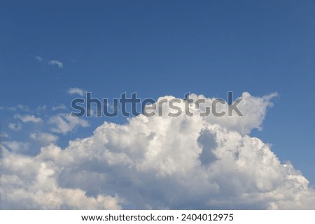 A large, pure white cumulus cloud, resembling a colossal mountain, set against the backdrop of a clear blue sky Royalty-Free Stock Photo #2404012975