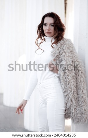 ~A beautiful woman walks around the city, wearing white clothes and an eco-skin faux coat