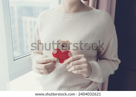 Small cute felt bear holding red heart in woman's hands close up Valentines Day