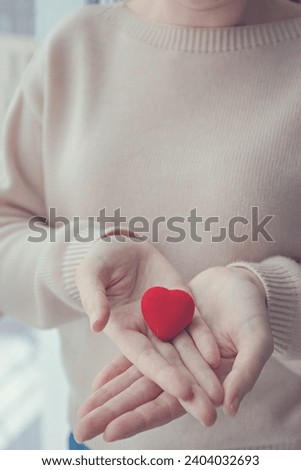 Woman holding small red heart in hands symbol of support, love, volunteering