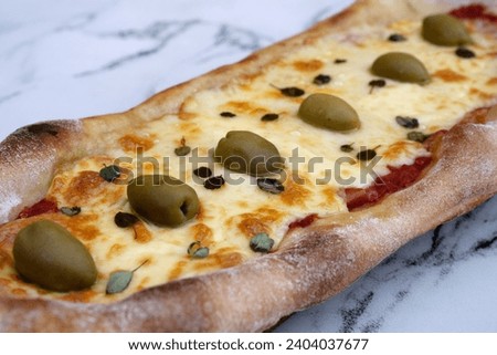 Closeup view of a mozzarella cheese pizza with olives and fresh oregano leaves, on the white marble table.