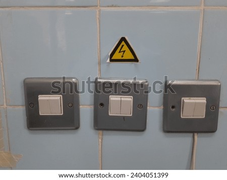 A yellow triangle sticker with a black lightning sign, electric hazard sign above, electrical connections, buttons and electrical sockets on the wall