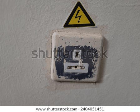 A yellow triangle sticker with a black lightning sign, electric hazard sign above, electrical connections, buttons and electrical sockets on the wall
