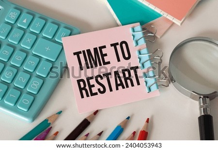Time to Restart text on a card on a paper clip on a white table next to a pen and a calculator