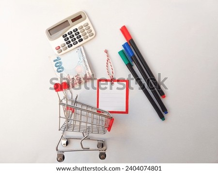 Hundred Turkish lira, blank note paper, shopping trolley, calculator on white flat lay Royalty-Free Stock Photo #2404074801