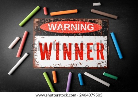 Winner. Metal warning sign and colored pieces of chalk on a dark chalkboard background.