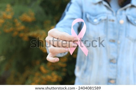 Woman in denim jacket holding pink awareness ribbon outdoors Royalty-Free Stock Photo #2404081589