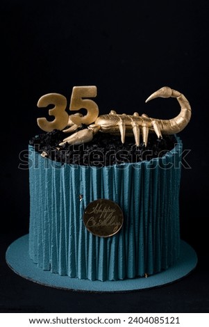 Cake with turquoise chocolate icing in the shape of corrugated paper decorated with edible golden scorpion on top. Birthday cake for a Scorpio sign of the zodiac on the black background