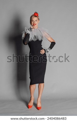 Elite clown. Woman dressed as clown iblack dress with harlequin collar and red hat. Contrast image on grey background. High quality photo