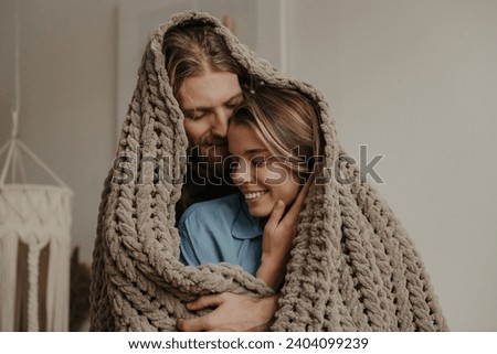 Beautiful young loving couple covering with a cozy warm blanket while spending time at home together Royalty-Free Stock Photo #2404099239