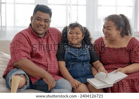 mother and girl are reading a book in living room. Asian chubby family relaxing with education program.