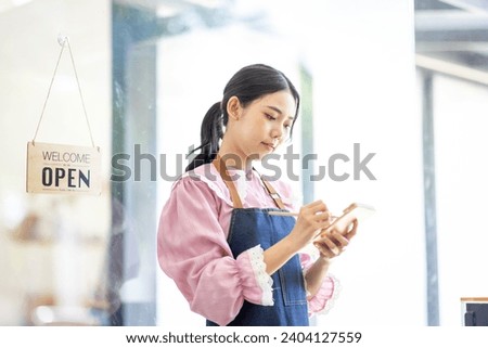 Portrait of happy waitress standing at restaurant entrance. SME entrepreneur young business asian woman attend new customers near door. Smiling small business owner showing open sign in her shop.