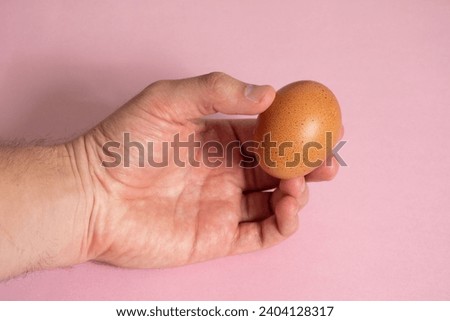 Left hand holding an egg on a pink background