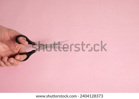 
Hand holding black hairdressing scissors on pink background