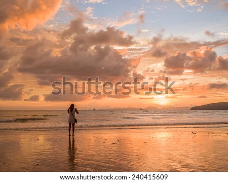 Woman taking pictures of the sunset on the beach of Ao Nang in Krabi Thailand