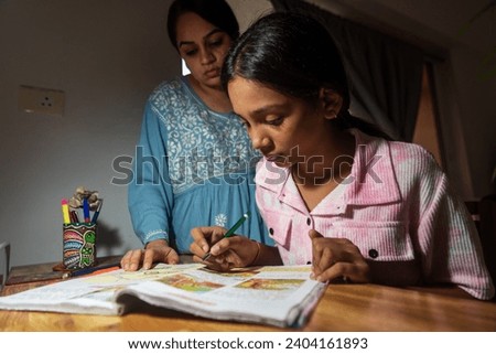 An Indian mother, wearing a blue chikankari kurta, supervises her pre-teen daughter's homework in the evening after returning from work at their home in Mumbai, India.
