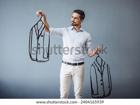 Handsome man in smart casual wear is holding drawn men suits and choosing between, on gray background