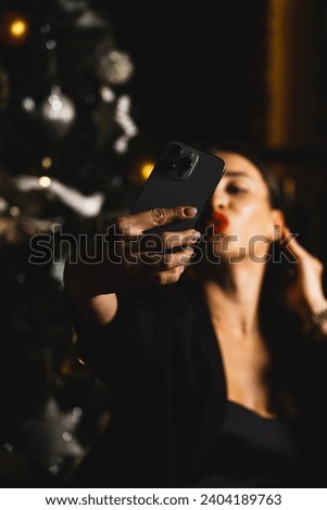 A pretty woman in a black suit takes a selfie against the background of a New Year tree. A woman takes a photo of herself. Christmas and New Year celebration concept