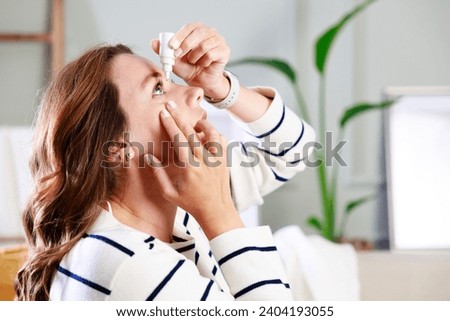 Young woman putting eye drops at home  Royalty-Free Stock Photo #2404193055