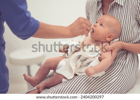Pediatrician administring oral vaccination against rotavirus infection to little baby in presence of his mother. Children health care and disease prevention. Royalty-Free Stock Photo #2404200297