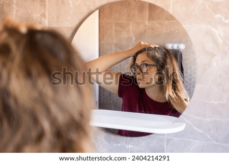 Woman Looking for Gray Hair in the Mirror. Young woman scared of premature aging signs