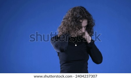 Stressed young woman rubbing neck trying to appease mental anguish while standing on blue background Royalty-Free Stock Photo #2404237307