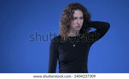 Stressed young woman rubbing neck trying to appease mental anguish while standing on blue background Royalty-Free Stock Photo #2404237309