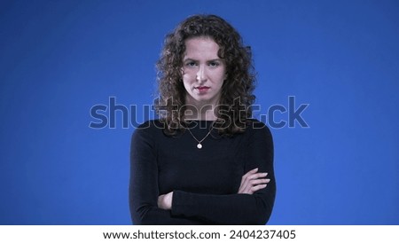 Upset woman with arms crossed looking at camera with angry expression, standing on blue background. Female person in 20s with negative body language Royalty-Free Stock Photo #2404237405