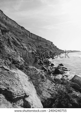 Black and white photo with a landscape of sandy and stony rock on the left and the sea on the right.